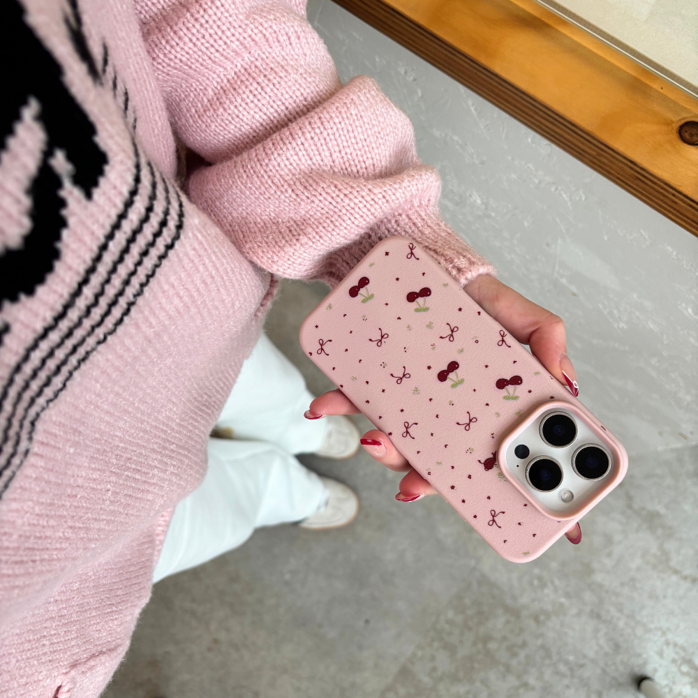Pink Coconut Lane phone case with ditsy bows and cherries, held by person in pink sweater, white pants, and shoes.