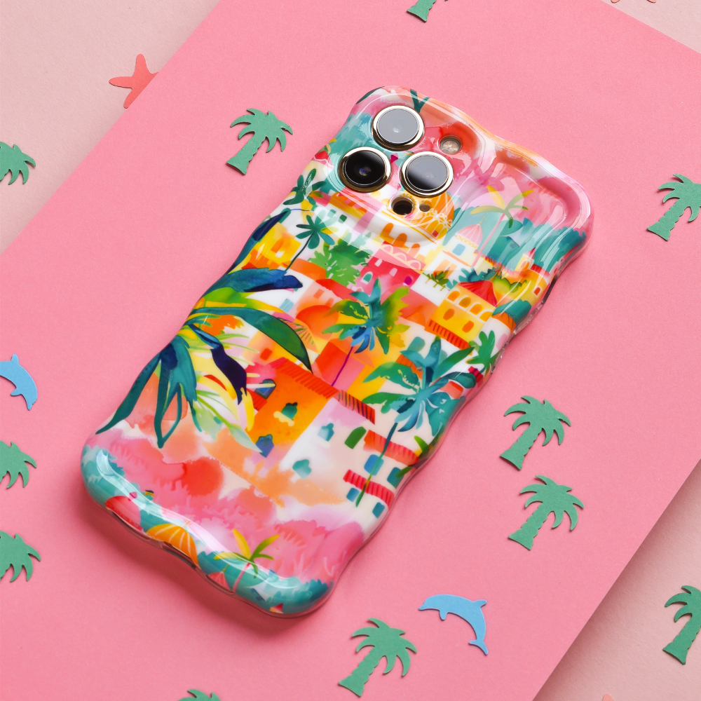 The Wavy Phone Case - Portofino Dreams by Coconut Lane, featuring a vibrant and colorful design adorned with tropical-themed drawings of palm trees, buildings, and abstract patterns, sits on a pink surface. This extra protective Italian seaside design is set against a background sprinkled with small cutouts of green palm trees and a blue dolphin.
