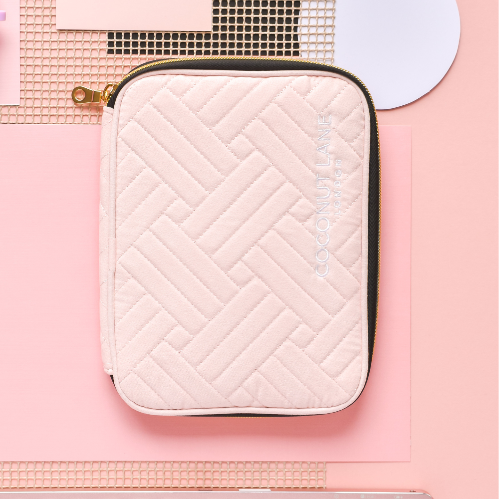 A Watch Strap Travel Case from Coconut Lane, featuring a pink quilted zippered design with a herringbone pattern, is placed on a pastel pink geometric background. "Coconut Lane" is printed in white text.