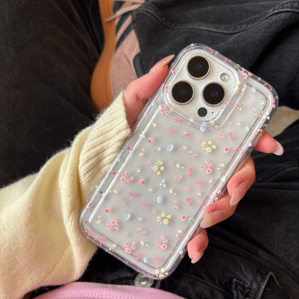 Clear Coconut Lane phone case with pink, yellow, and blue floral pattern held in a hand.