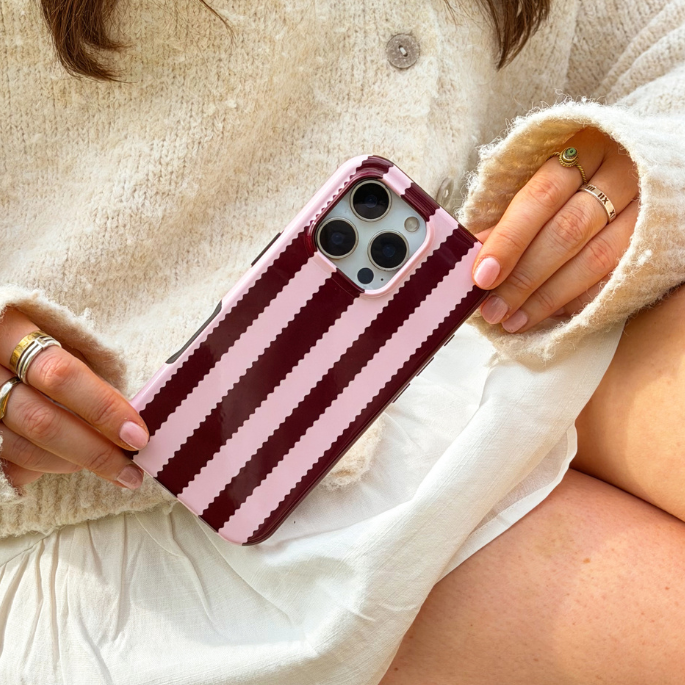 Girl sat in field with blushberry scallop stripes tough phone case in hand wearing cream outfit