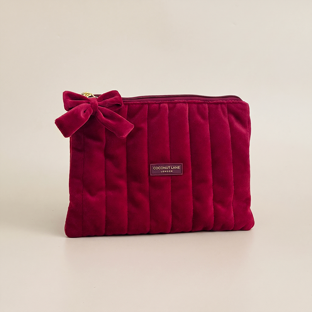 Burgundy velvet cosmetic bag with a quilted design, bow detail, and gold-tone hardware.