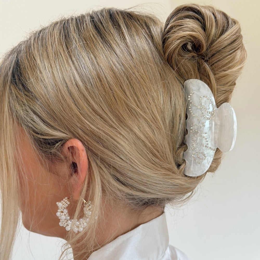 Blonde hair styled in an updo with a decorative bride claw clip on a plain background