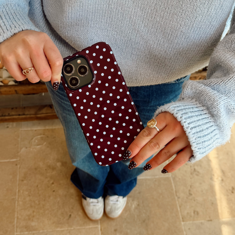 Girl holding her brown and blue polka dot tough phone case wearing a blue sweater with matching nails