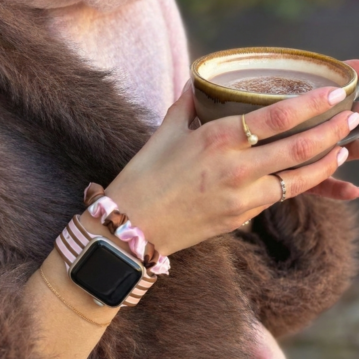 Pink and Brown stripes silicone sport band, attached to a black Apple Watch smartwatch on a woman's wrist alongside a matching cocoa and pink striped satin scrunchie.