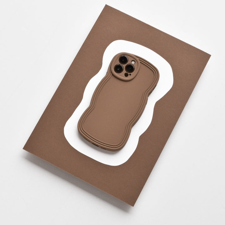 A smartphone with the NAKD Curvy Phone Case - Coffee by Coconut Lane sits on a white paper cutout, which rests atop a larger rectangular brown surface. The entire setup is on a light gray background.
