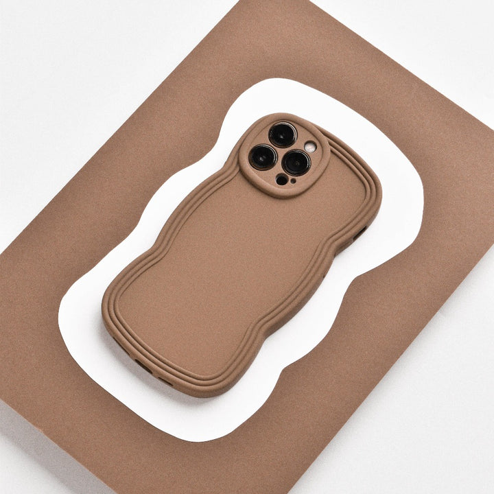 A lightweight, brown NAKD Curvy Phone Case - Coffee from Coconut Lane with a wavy design lies on a flat, brown and white, wavy-edged surface. The case has precise cutouts for the camera lenses and appears highly protective. The background contrasts with the NAKD Curvy Phone Case, highlighting its unique shape and design.