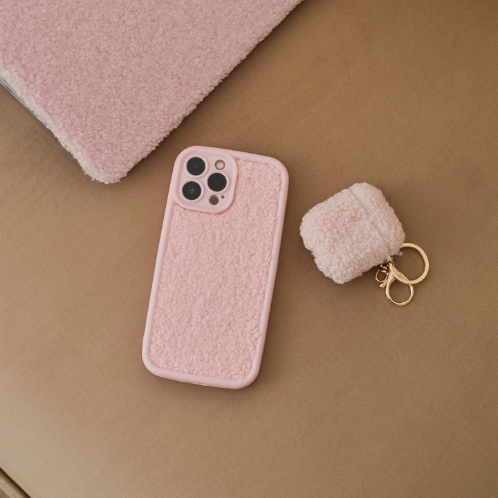 A Cosy Teddy Phone Case - Pink by Coconut Lane, complete with a matching keychain pouch, is placed on a light brown fabric surface. This textured teddy case features camera cutouts for a multi-lens setup, and the keychain comes with gold rings for added convenience and style.