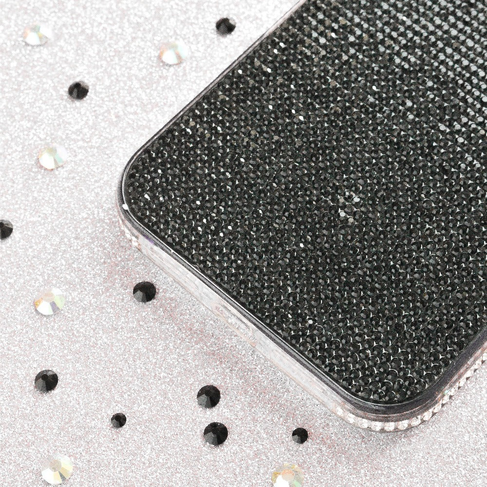 A close-up of a smartphone encased in Coconut Lane’s Disco Sparkle Phone Case - Black, resting on a silver, glittery surface. Both the extra protective case and the surface are adorned with scattered round, shimmering rhinestones.