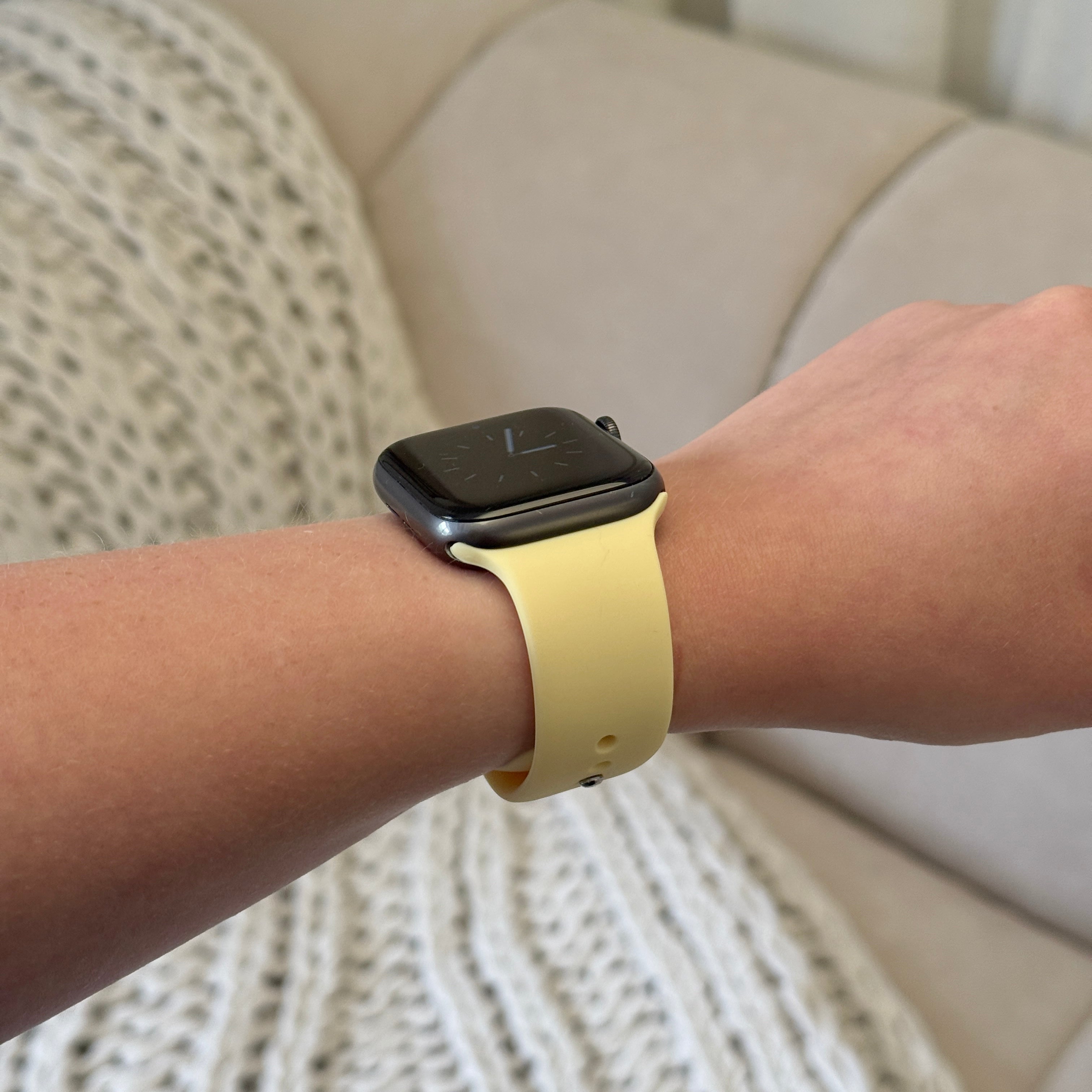 Black smartwatch with a yellow Coconut Lane NAKD Apple Watch strap, worn on a beige couch.