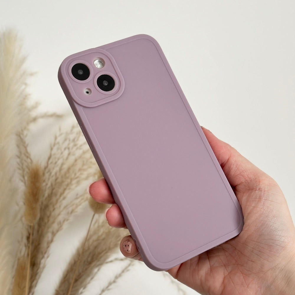 A hand holding a smartphone with a Coconut Lane NAKD Phone Case in lilac from the spring collection. The phone, boasting full camera protection with two rear lenses, is set against a background of beige pampas grass, creating a minimalistic and aesthetically pleasing composition perfect for pastel favorites.