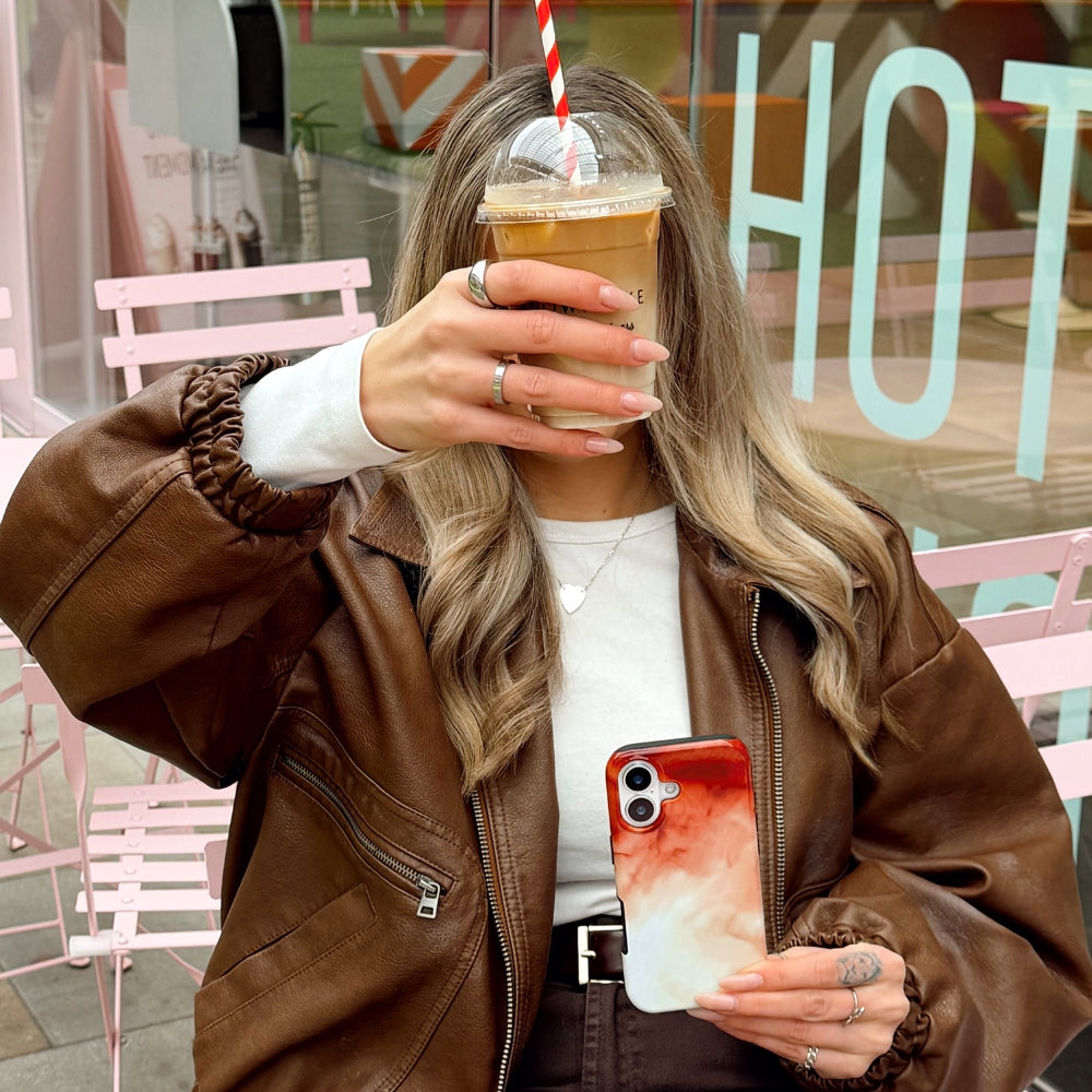 Girl taking a selfie with iced coffee and matching phone case in an outdoor setting.