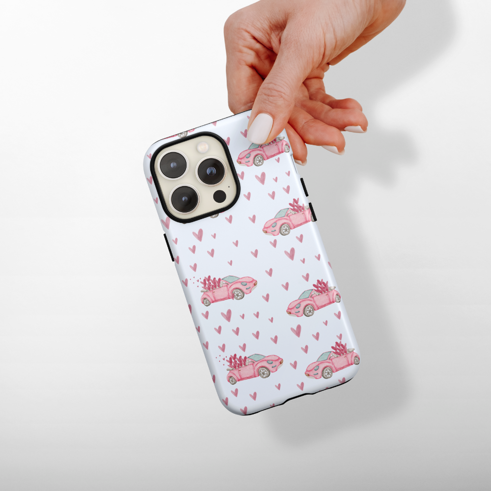 Phone case with pink car and heart pattern held by a hand on a white background