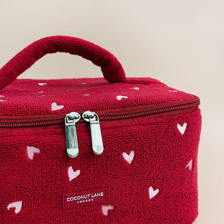 Red cosmetic bag with heart patterns and 'Coconut Lane' branding on a beige background