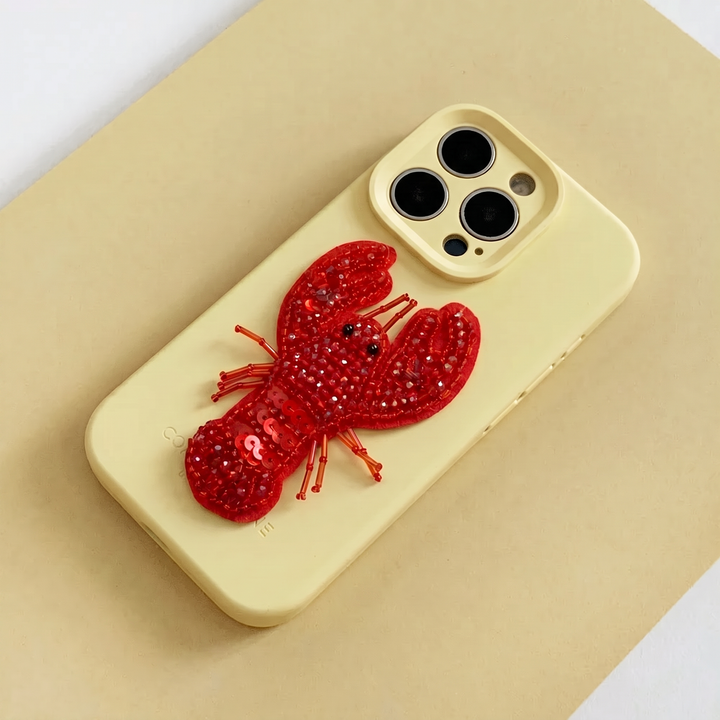 Red 3D Lobster made from beads and sequins, on top of a yellow Coconut Lane Phone Case. 