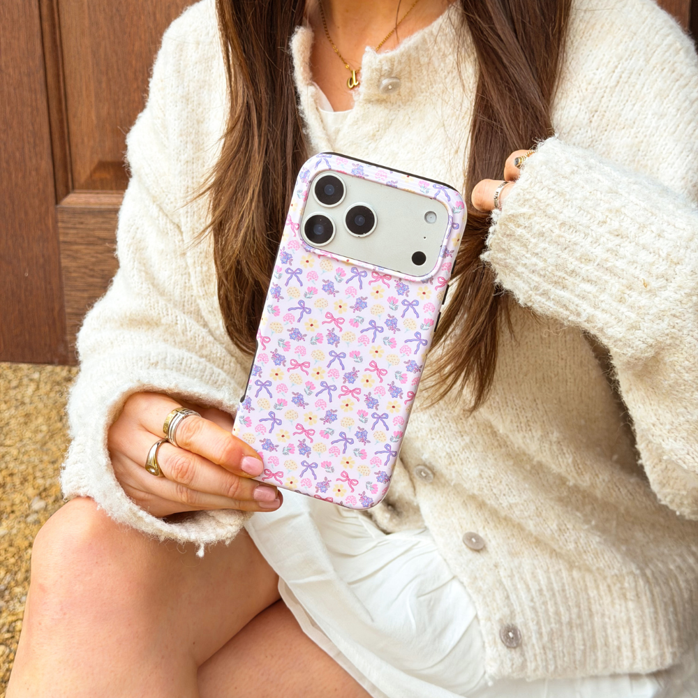 Girl in cream cardigan holding her purple phone case with bows and flowers on it called spring bows tough magsafe phone case