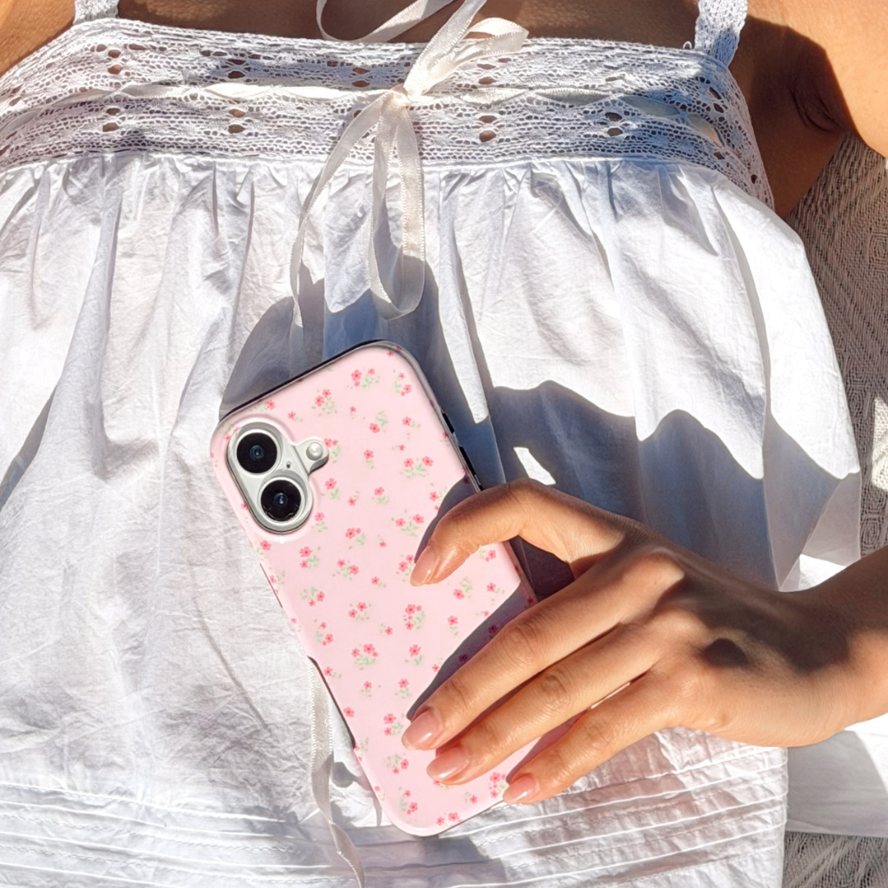 Person in white dress holding a pink Coconut Lane Tough Phone Case with small floral pattern in sunlight.