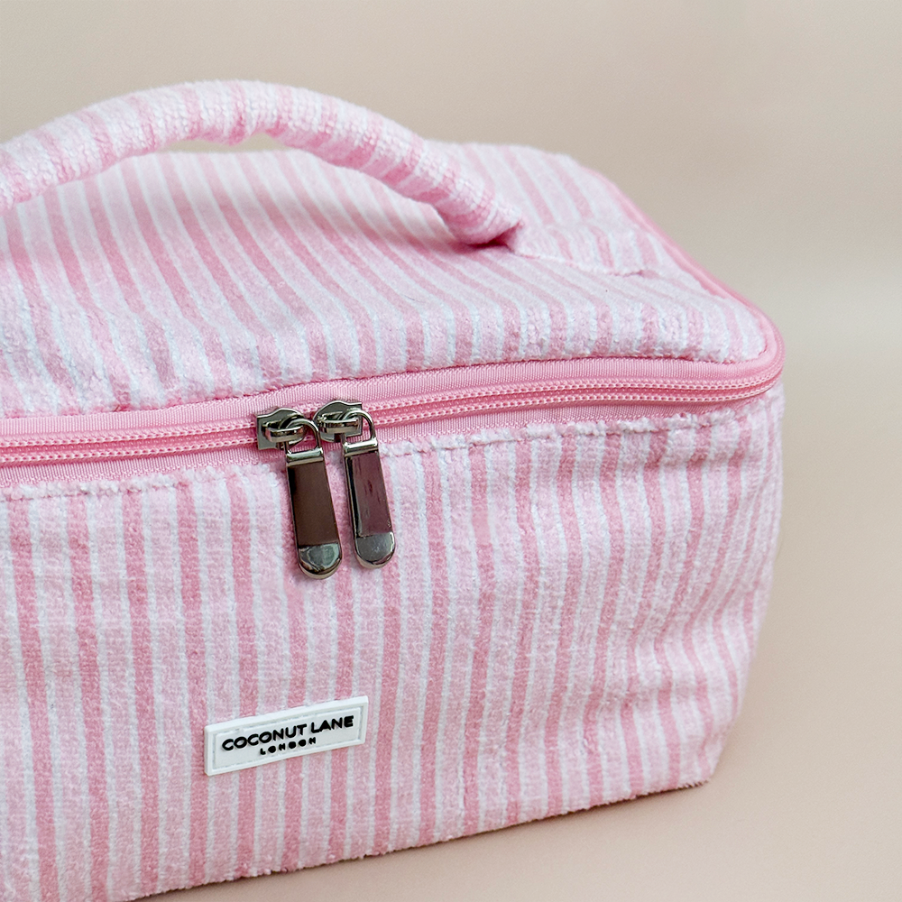 Pink striped toiletry bag with Coconut Lane brand label on a beige background