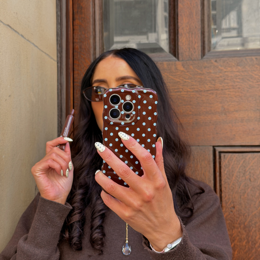 Girl applying lipgloss holding her wavy brown and blue polka dot phone case