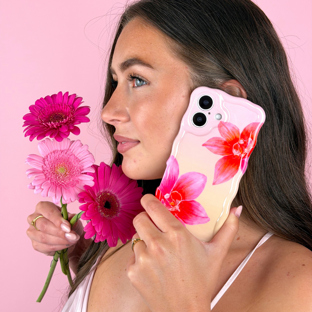 Woman holding a phone with a floral case against a pink background