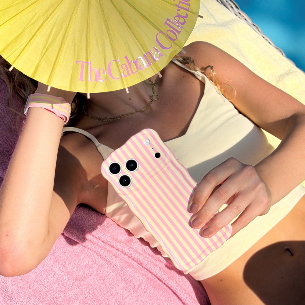 Girl holding a phone with a pink and yellow striped pink lemonade case under a yellow umbrella with 'The Cabana Collection' text.