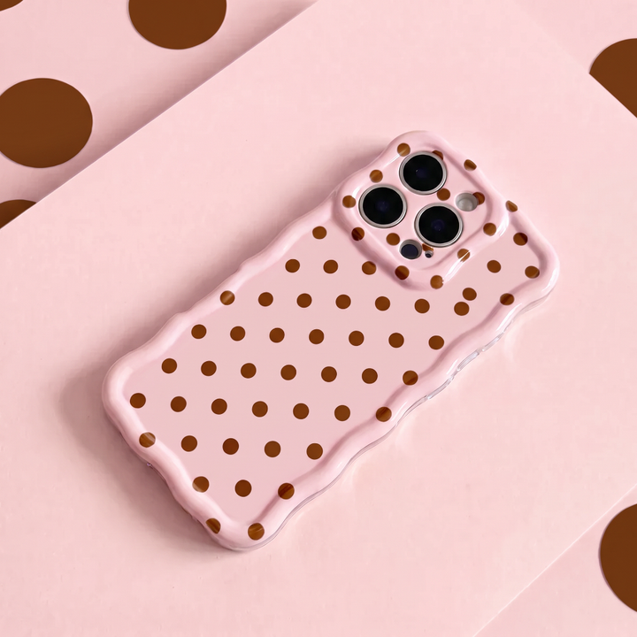 Pink Wavy Phone Case featuring a glossy blush pink finish with brown polka dots, scalloped edges and triple camera cutouts, displayed on a matching pink background.