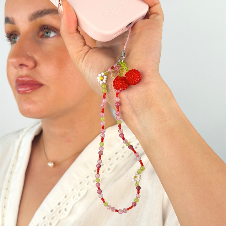 Girl holding phone case by her face in the studio showing her cherry bomb phone strap