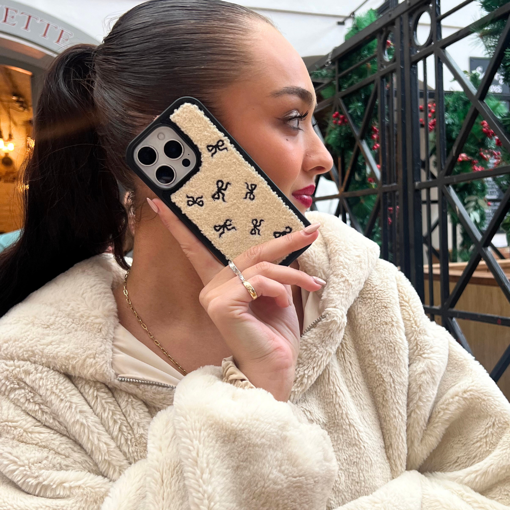 Cream boucle phone case with black bow pattern, held by woman wearing a beige fleece.