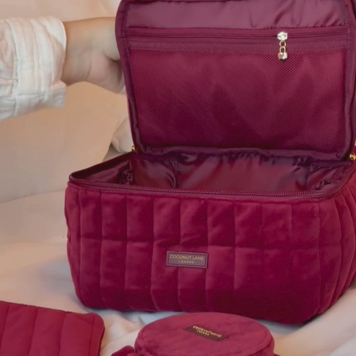 Burgundy velvet cosmetic bag with a quilted design, top handle, bow detail, and gold-tone hardware.