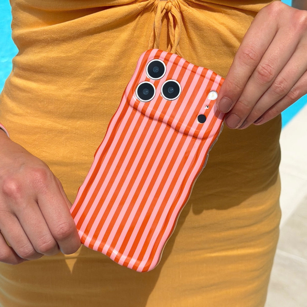 Phone case with orange and pink striped pattern held by a person against a yellow dress, standing by pool