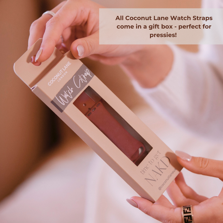 A person wearing a light-colored top is holding a boxed Coconut Lane NAKD Apple Watch Strap. The boxed watch strap is olive green and from the NAKD Collection, featuring the tagline "time to get NAKD." A text overlay reads, "All Coconut Lane Watch Straps come in a gift box - perfect for pressies!