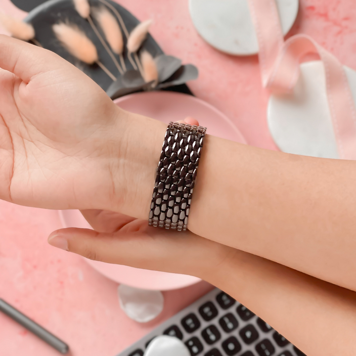 A person is wearing a Mermaid Apple Watch Strap - Black by Coconut Lane on their wrist. The background features various soft pink and white items, including a ribbon, dried flowers, a keyboard, and bowls, creating an aesthetically pleasing, cozy setting.