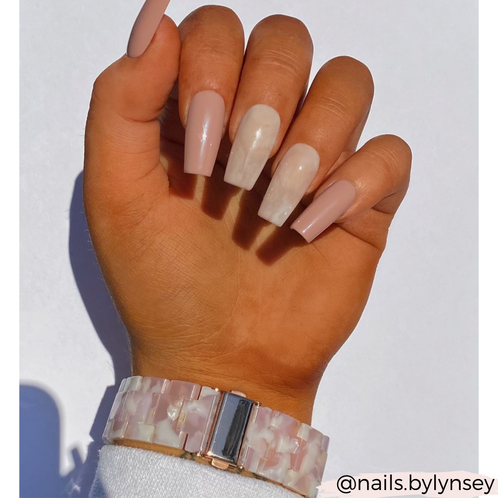 A hand showcases long, polished acrylic nails featuring neutral and white marble designs. The wrist is adorned with Coconut Lane's Luxe Rose Apple Watch Strap, which has a pearl-like band. The image is set against a plain white background, with the text "@nails.bylynsey" in the bottom right corner.