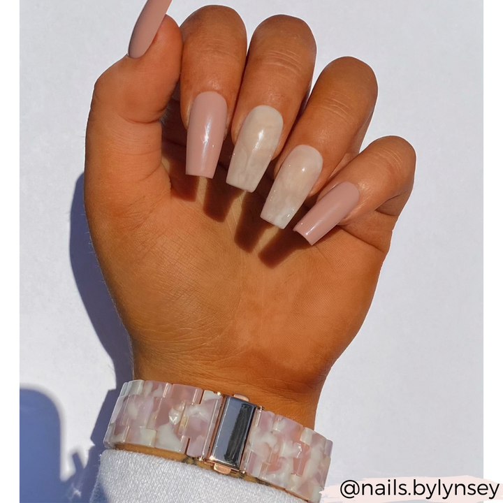 A hand showcases long, polished acrylic nails featuring neutral and white marble designs. The wrist is adorned with Coconut Lane's Luxe Rose Apple Watch Strap, which has a pearl-like band. The image is set against a plain white background, with the text "@nails.bylynsey" in the bottom right corner.